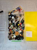 Large clear plastic bin filled with a variety of buttons of different sizes and colors with a yellow lid beside it.