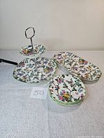 Full view of chintz dessert set including two-tier serving tray, large round plate, rectangular platter, and five small plates stacked.