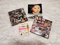 Four collector books on a white lace tablecloth. Books are about vintage decor, cloth dolls, and Barbie dolls.