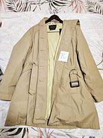 Full view of the tan Eddie Bauer goose down jacket laid flat on a floral background, showing overall condition and design including adjustable side buckle belt and pockets.