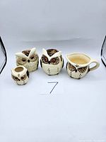 Front view of the four owl ceramic owl pitchers and creamer set with vintage wear, labeled number 7 in photos