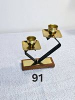 Front view of vintage signed Etch Teakholz Germany MCM candle holder featuring two brass candle cups on a zigzag black arm and rectangular wooden base with brass inset.