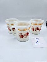 Three white opaque glass Fire King mugs with mid-century modern red and orange geometric pattern, displayed together.