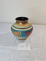 Front and side view of round German pottery vase with colorful hand-painted designs and glossy black interior.