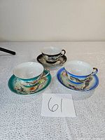 Photo of three dragonware teacup and saucer sets in turquoise green, blue, and dark brown backgrounds arranged on table