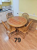 Photo of round wooden kitchen table with tiled top and four matching wooden chairs in a kitchen setting.