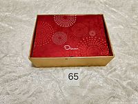 Closed gold box with red and white circular dot design labeled 'Oscar' on top
