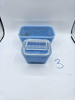Two blue Pyrex rectangular glass containers, one large and one small, with matching clear ribbed lids. Both containers show vintage wear.