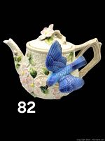 Front and side view of Fitz and Floyd teapot showing basketweave texture, pink flowers, green leaves, and bluebird applique
