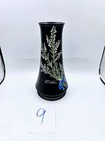 Front view of Shelley England ceramic vase showing the black matte finish, hand-painted white flowers, green foliage, and blue ribbon detail with 'For Luck Frae Edinburgh' text.