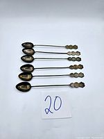 Six vintage sterling silver souvenir spoons laid flat on white background with paper labeled '20'
