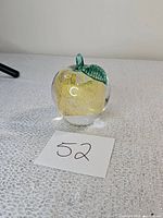 Front angled view of clear glass apple-shaped paperweight showcasing gold leaf inside and green glass leaf/stem
