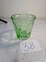 Front and side view of green uranium glass measuring cup showing its shape, embossed measurement marks, and decorative exterior pattern.