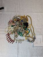 Vintage jewelry lot with mixed necklaces, brooches, and costume jewelry pieces showing various stones, beads, and chains, displaying overall condition and variety.