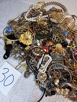 Photo showing a large pile of assorted vintage signed costume jewelry including gold-tone and faux pearl pieces, rings, brooches, and earrings.