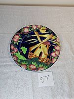 Top view of the vintage Maling pottery plate showing the windmill and floral design in good lighting on a white textured surface with lot number 57.