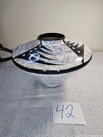 Side view of the wide round vintage ceramic vase showing abstract black and eye-like designs on a mottled blue-white background.