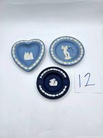 Three Wedgwood jasperware small plates/dishes on a white background. One heart-shaped and two round, with classical white relief decorations on blue and dark blue bases.