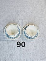 Two vintage Wedgwood Queensware teacups with matching saucers, blue floral pattern on white ceramic, finished with some wear due to age.