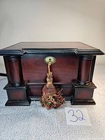 Closed front view of the wood jewelry box with decorative columns and tassel on the lock.