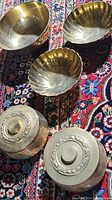 All five brass dishes arranged on a patterned carpet showing two lidded containers and three bowls, two of which have scalloped edges.