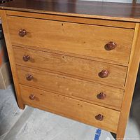 Front view of antique dresser showing four wooden drawers with round wooden knobs and a worn top surface.