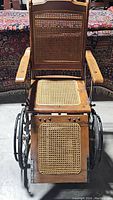 Front view of the wooden antique wheelchair showing cane seat, backrest, and leg rest panels.