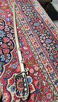 Full length view of vintage military sword in metallic scabbard on patterned rug.