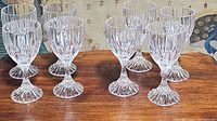 Eight clear crystal stemware glasses arranged in two rows on wooden surface showing vertical ribbed design and flared foot.