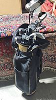 Full view of black and tan golf bag filled with various golf clubs placed on a patterned rug.