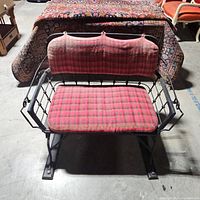 Front view of black wrought iron and wood bench with red and black plaid removable cushions on seat and back