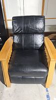 Front view of black leather recliner chair with wooden armrests and padded leather seat and back