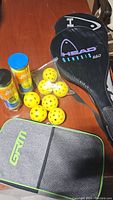 Pickleball rackets, yellow perforated pickleballs, and paddle case arranged on wooden surface.