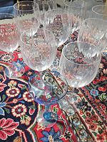 Photo showing nine clear glass goblets and one clear goblet with blue stem and base on a colorful patterned carpet.