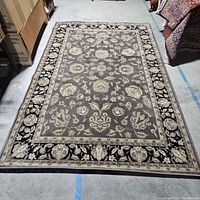 Full view of traditional rug showing pattern and colors black, cream, and brown on a 7x9 base