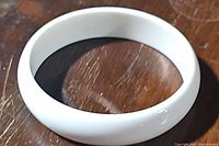 Solid white bangle bracelet shown to highlight smooth glossy finish and round shape.