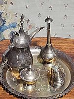 Full set displaying a vintage brass drinking set on a round engraved tray on a wooden surface.