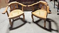 Pair of two vintage wooden armchairs shown front angled with carved backs and cane woven seats on a concrete floor.