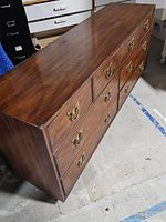 Full view of the dresser showing seven drawers with brass handles, brown wood finish, minor scratches on surface.