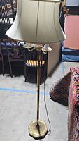 Full view of vintage brass floor lamp with beige fabric lampshade and two bulb sockets, standing on hexagonal base.