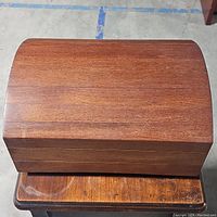 Top view of closed wooden jewelry box with curved lid, showing wood grain and surface wear.