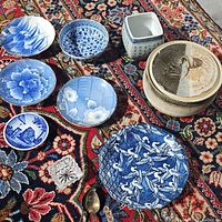 Overview of the assortment of vintage blue and white serving dishes, a ceramic pot with lid and small dish on a patterned carpet