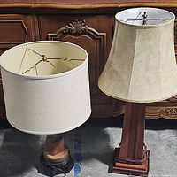 Both lamps shown side by side with fabric shades, placed on concrete floor in front of wooden furniture.