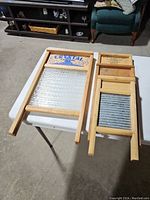 Four vintage washboards on folding table, one large with glass ribbed surface and three smaller with metal ribbed surfaces