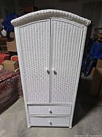 Front view of white wicker wardrobe cabinet with two doors and two drawers at bottom.