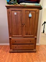 Front view of the wooden armoire showing two raised panel doors on the upper section and two drawers below with wooden knobs.