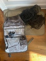 Photo showing all items together: four rectangular beige floor mats, two black cargo nets, and one travel organizer bag with mesh and zippered pockets.