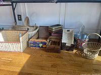 Photo of approximately a dozen wicker baskets and wood and metal containers arranged on floor under table.