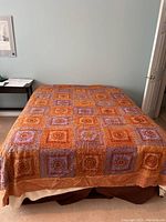 Full view of the Full/Queen size bedspread on an unmade bed showing the overall patchwork design in orange, red, and purple squares.
