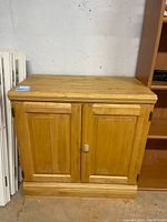 Front view of unfinished wood cabinet showing two paneled doors, one door knob present, one missing.